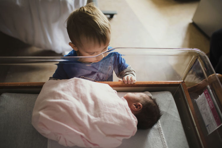 High angle view of brother looking at sister sleeping in crib