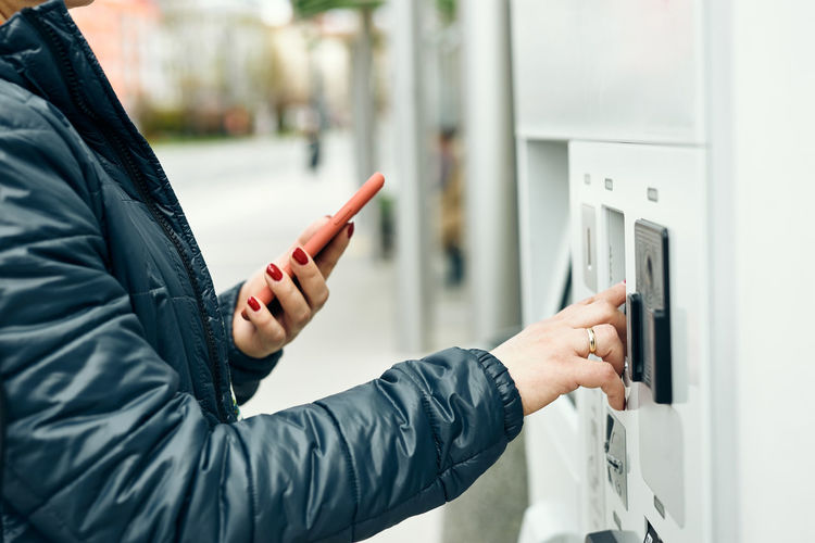 Woman buying ticket at ticket machine paying using mobile payment app on smartphone. buying tickets