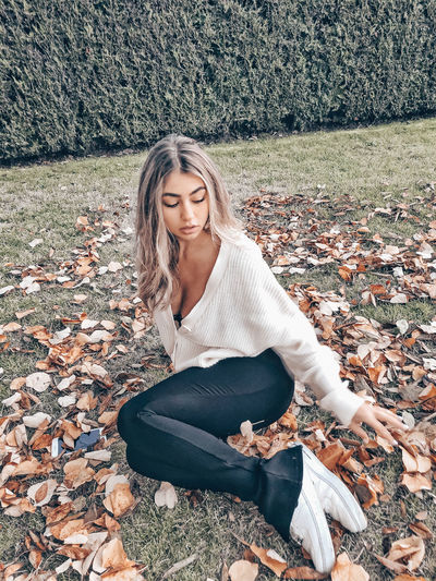 Beautiful young woman sitting on field during autumn
