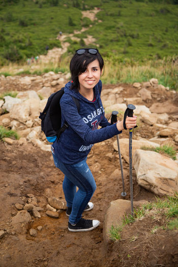 Portrait of smiling woman holding walking stick standing on dirt road