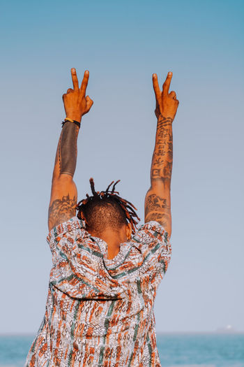 Low angle view of hand with tattoos by sea against clear sky