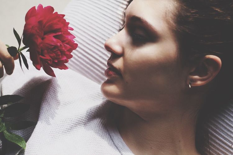 High angle close-up of young woman looking at flower while lying on bed