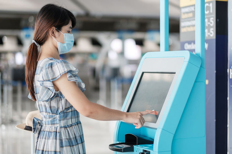 Side view of woman wearing mask using atm machine at airport