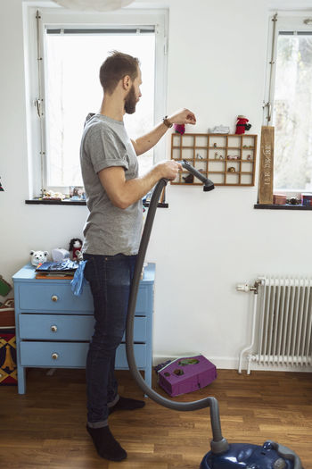 Full length of man vacuuming small shelves