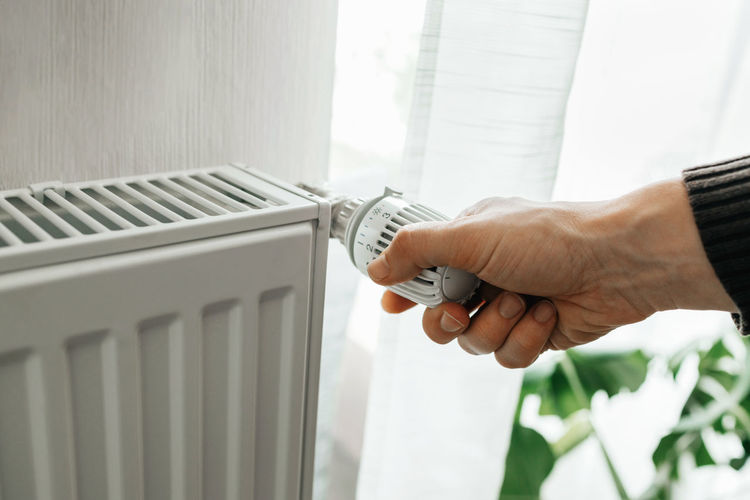 A man regulates the temperature on the radiator at home. rising prices for heating in households. 