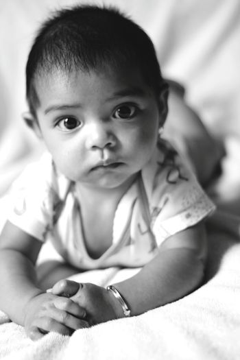 Close-up portrait of cute baby girl sitting on bed at home
