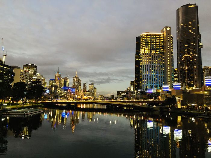 Illuminated melbourne skyline and buildings by river against sky in city at night