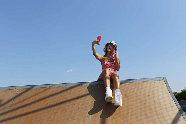 Happy woman gesturing and taking selfie through mobile phone on rooftop of house
