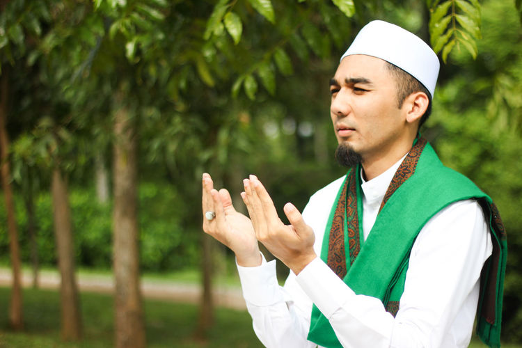 Man in traditional clothing praying against trees