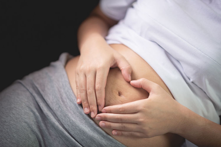 Midsection of woman making heart shape on pregnant belly