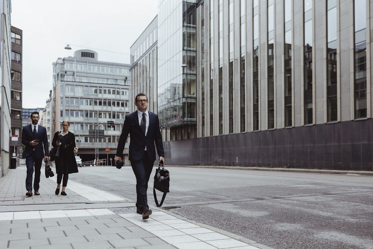 Male entrepreneur with bag walking ahead of coworkers in city