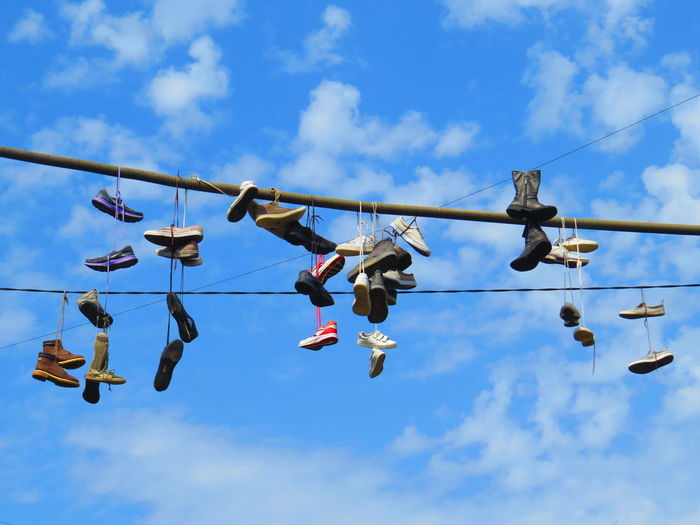 Low angle view of shoes hanging on cable against sky