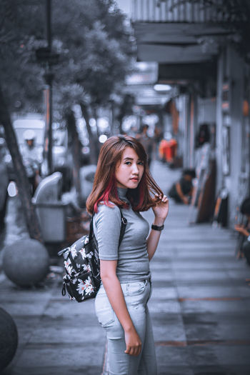 Portrait of young woman standing on footpath in city