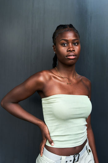 Self assured young african american female with long braids wearing tube top and looking at camera on gray background