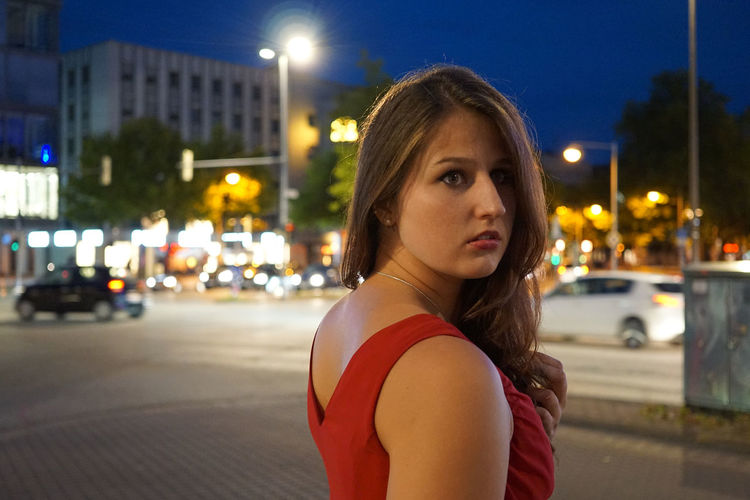 Young woman looking away while standing on city street at night