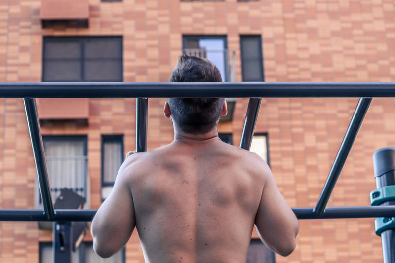 Rear view of shirtless man standing against railing
