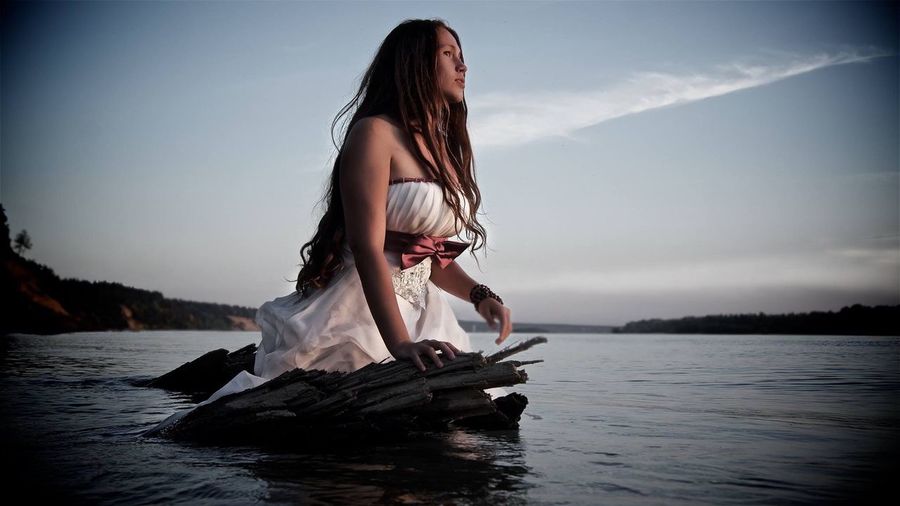 Young woman wearing white dress while standing in lake