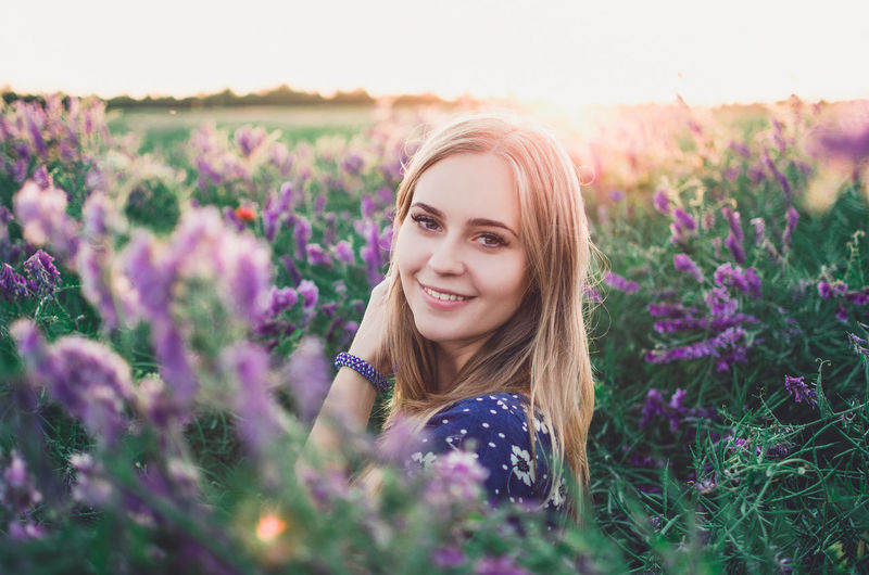 Portrait of beautiful young woman with purple flowers on field
