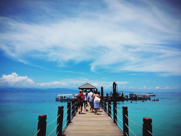 Rear view of people walking on jetty against sea