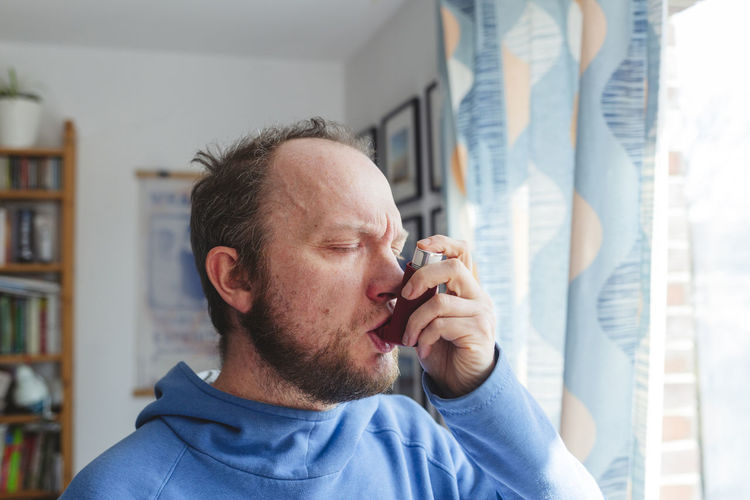 Man with eyes closed using asthma inhaler at home