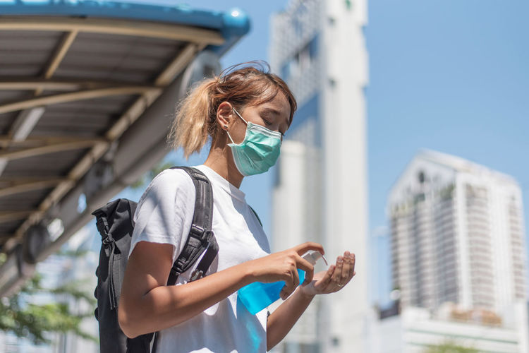 Young woman wearing mask washing hands in city