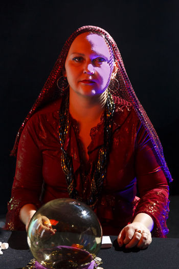 Portrait of young woman holding crystal ball against black background