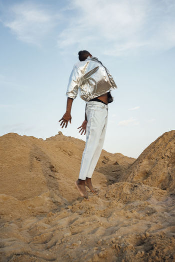 Man wearing silver jacket jumping on sand