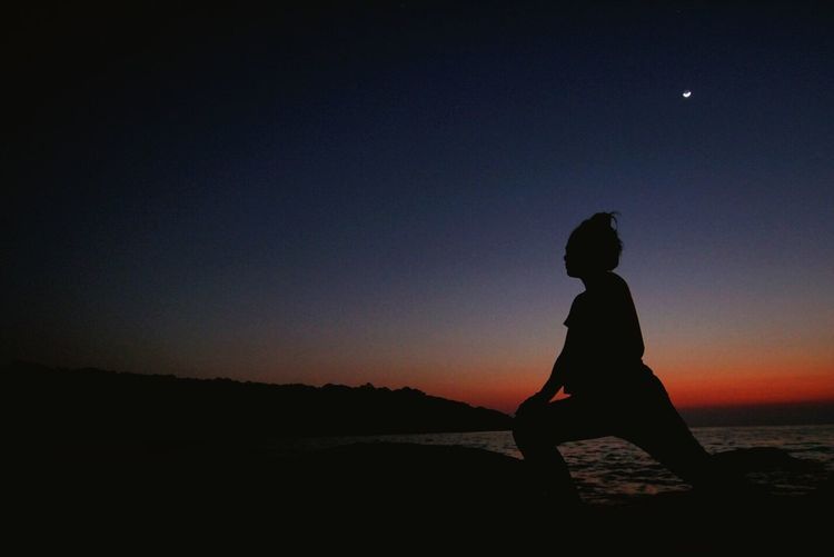 Silhouette woman doing yoga on shore at beach during sunrise