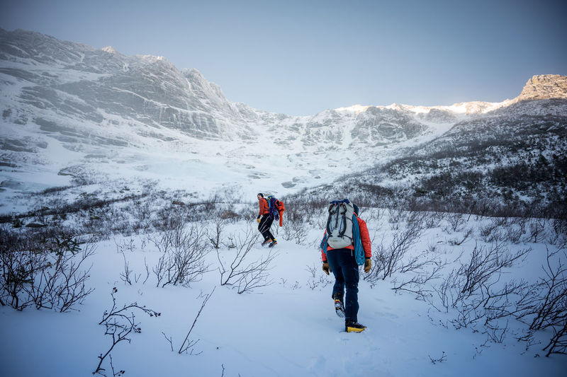 Two male climbers walk upwards towards a mountain ridge in winter