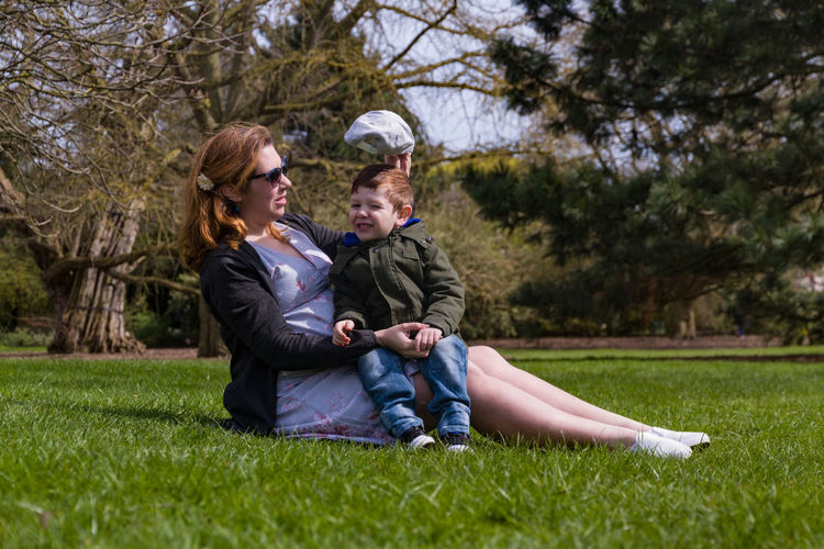 Full length of mother and son sitting on grass against trees