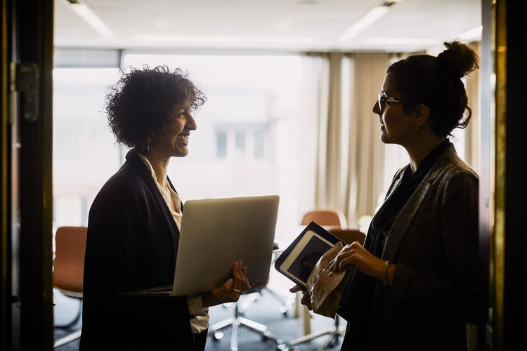Legal female coworkers with wireless technology discussing at doorway