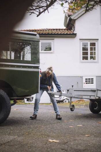 Mature woman towing trailer to sports utility vehicle on driveway