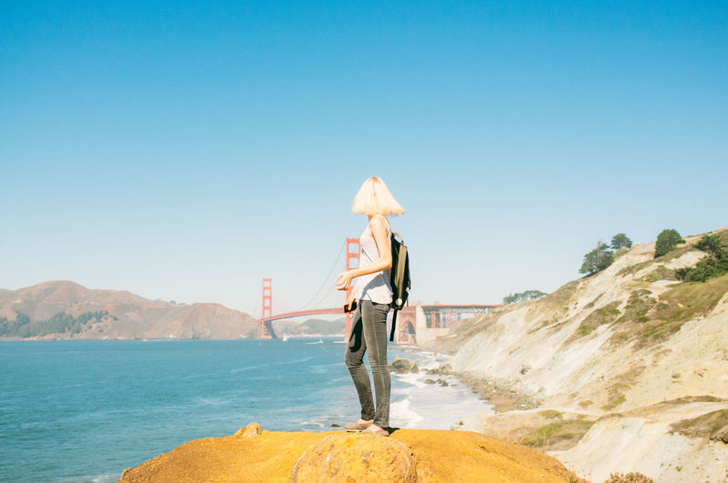 Side view of woman with backpack looking at golden gate bridge against sky