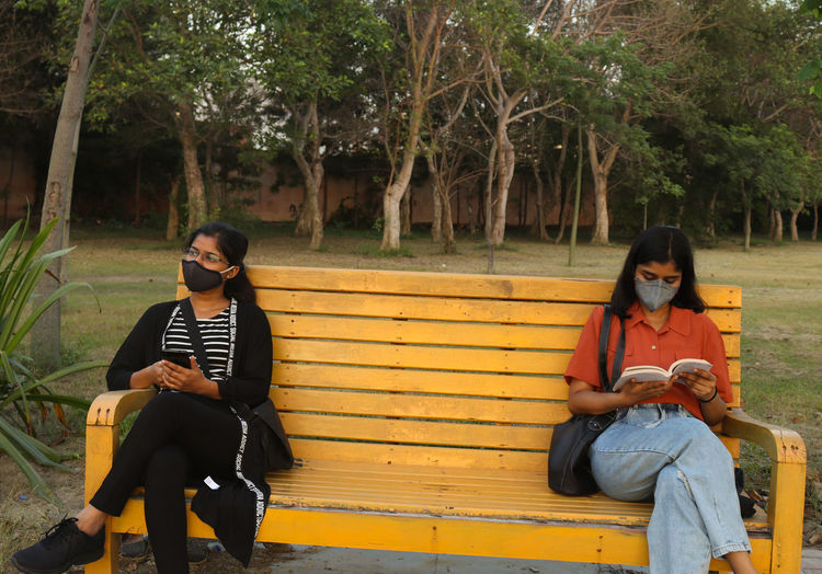 Young women wearing mask sitting on bench at park