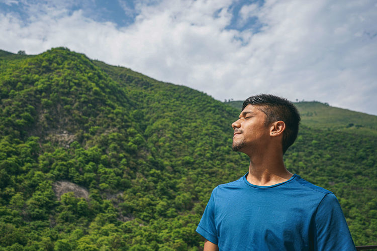 Young indian boy standing in the edge of the balcony, enjoying the scenic view of the green mountain