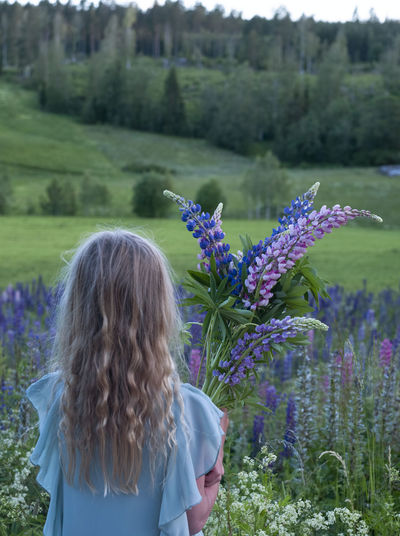 Rear view of woman with purple flowers on field