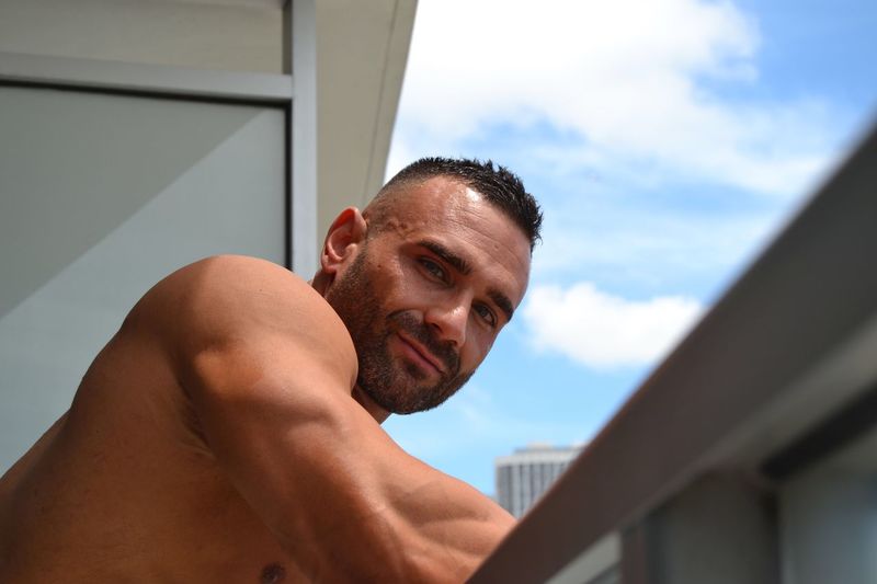 Low angle portrait of confident shirtless man standing in balcony