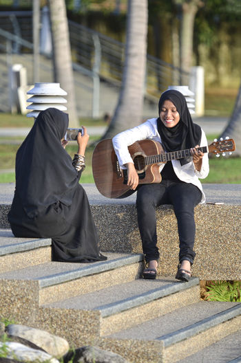 A girl playing the guitar while the other girl records it for social media. 