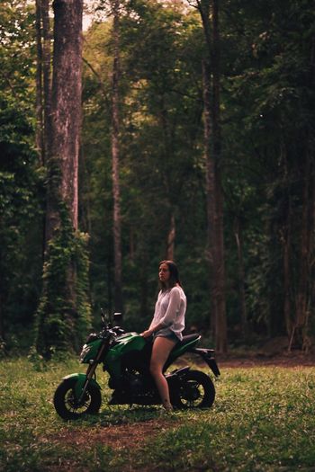 Side view of woman sitting on motorcycle at field in forest