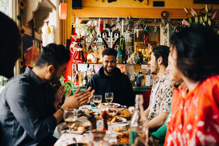 Cheerful young multi-ethnic friends enjoying brunch while sitting at table in restaurant