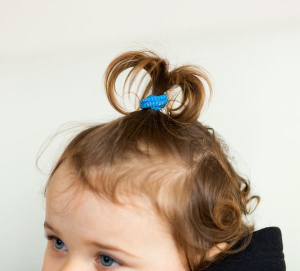 Close-up of baby girl with ponytail against wall
