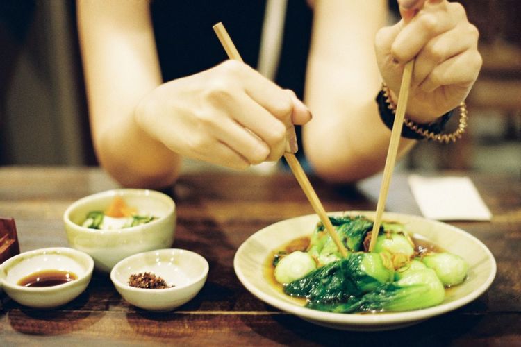 Midsection of woman using chopsticks while having food on table