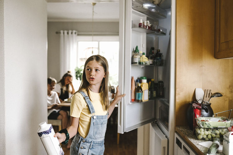 Caucasian girl with juice pack standing by refrigerator