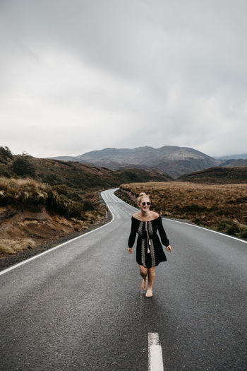Full length of cheerful young woman walking on road against cloudy sky