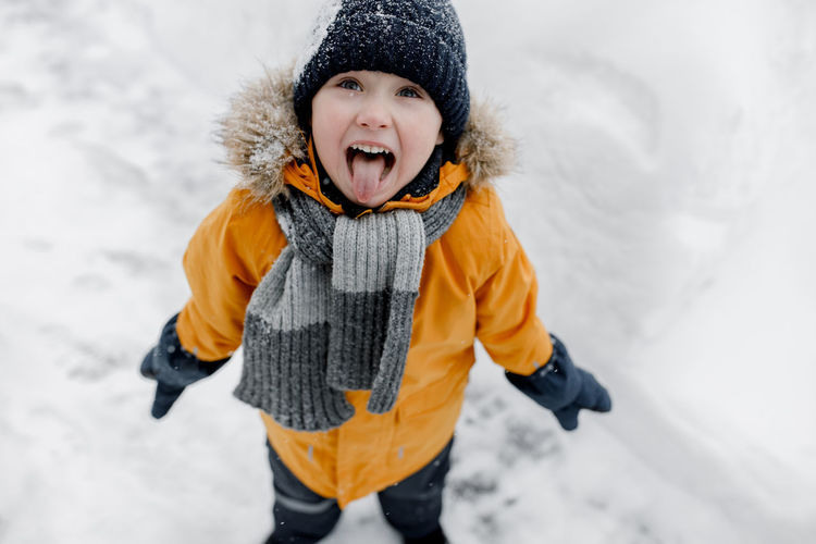 Charming little boy catches snowflakes with his tongue in a beautiful orange winter park
