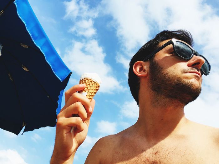 Low angle view of man holding ice cream against sky