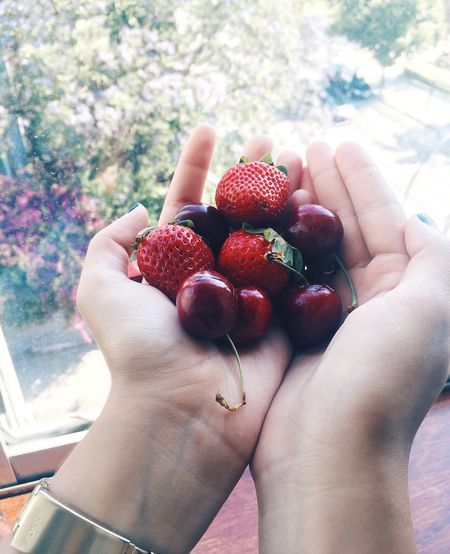 Close-up of cropped hands holding strawberries and cherries at home