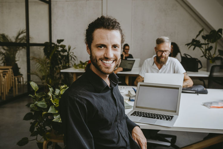 Portrait of smiling male entrepreneur sitting by laptop in office