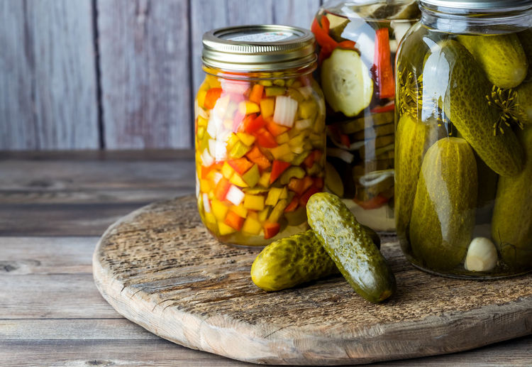 Jars of pickles and peppers against a wooden background.