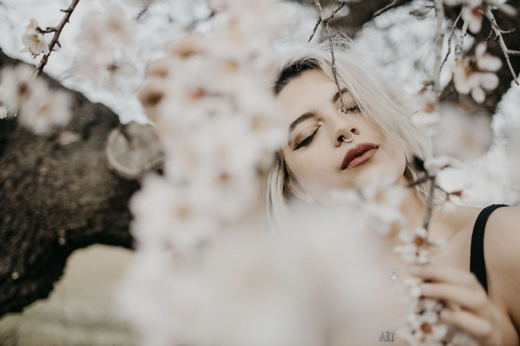 Young woman with eyes closed standing under blossoming almond tree